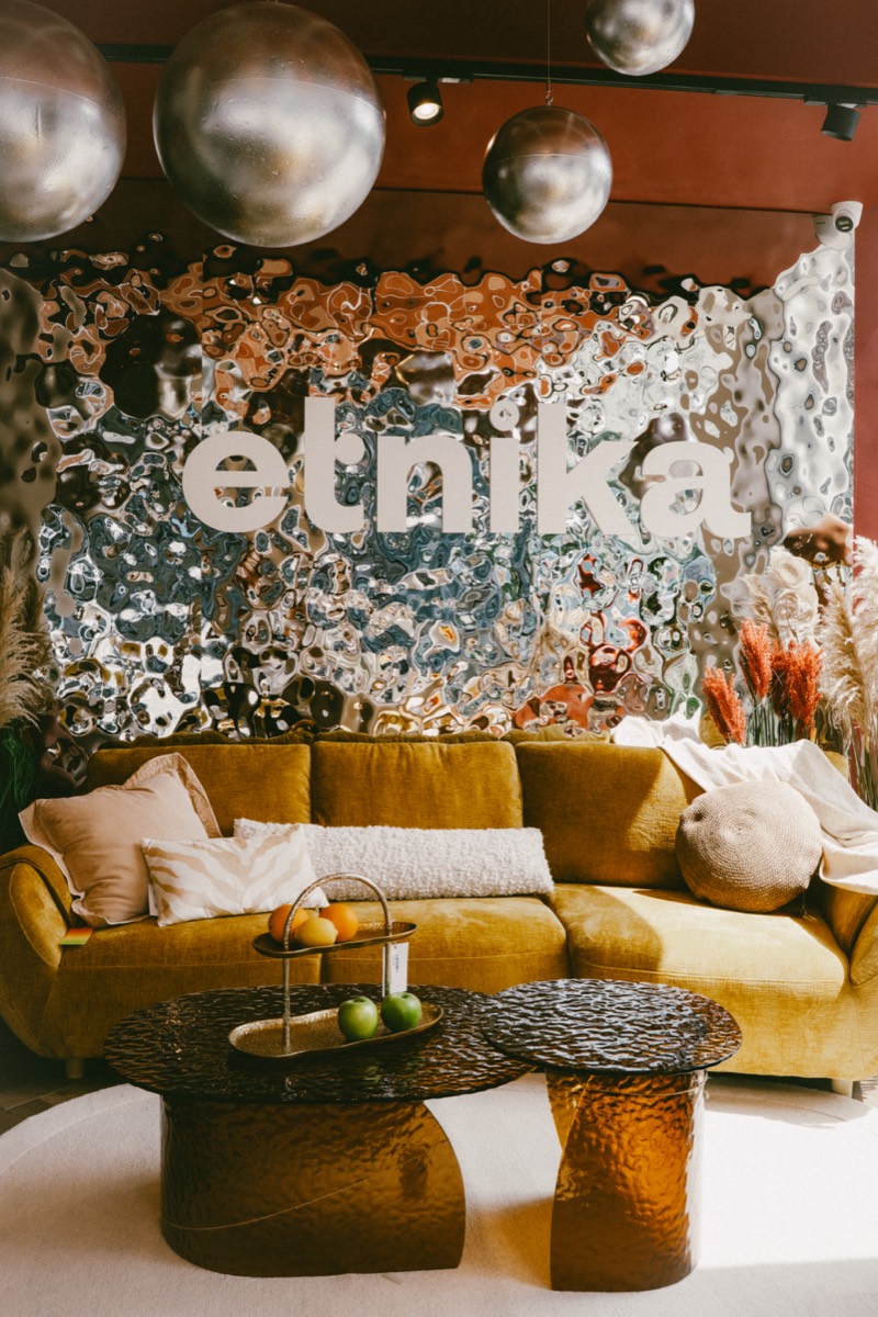 Musztardowa sofa i szklane stoliki pod ścianą z logo etnika